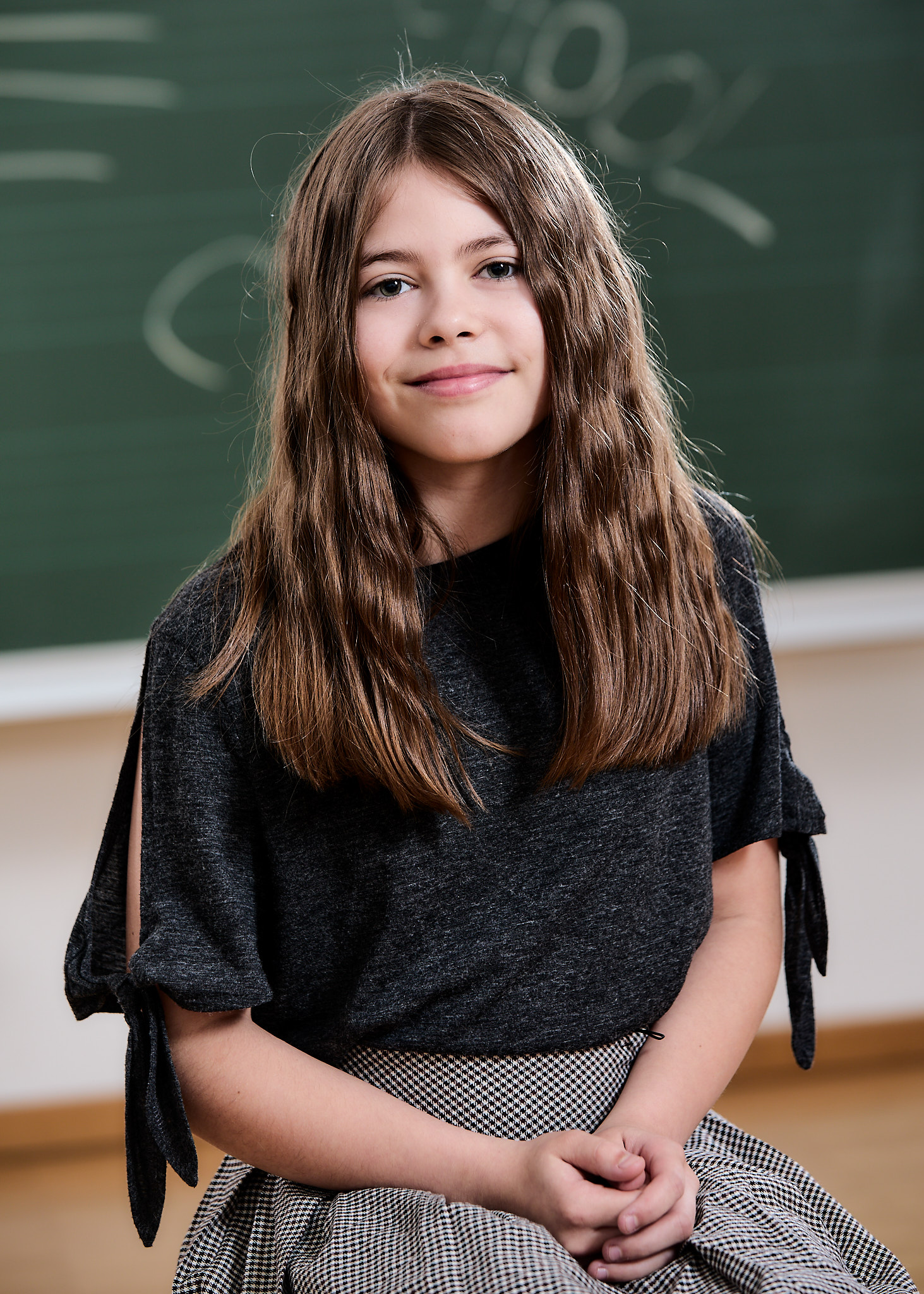 Portrait einer Schülerin, die vor der Schultafel sitzt. Schulfotografie.