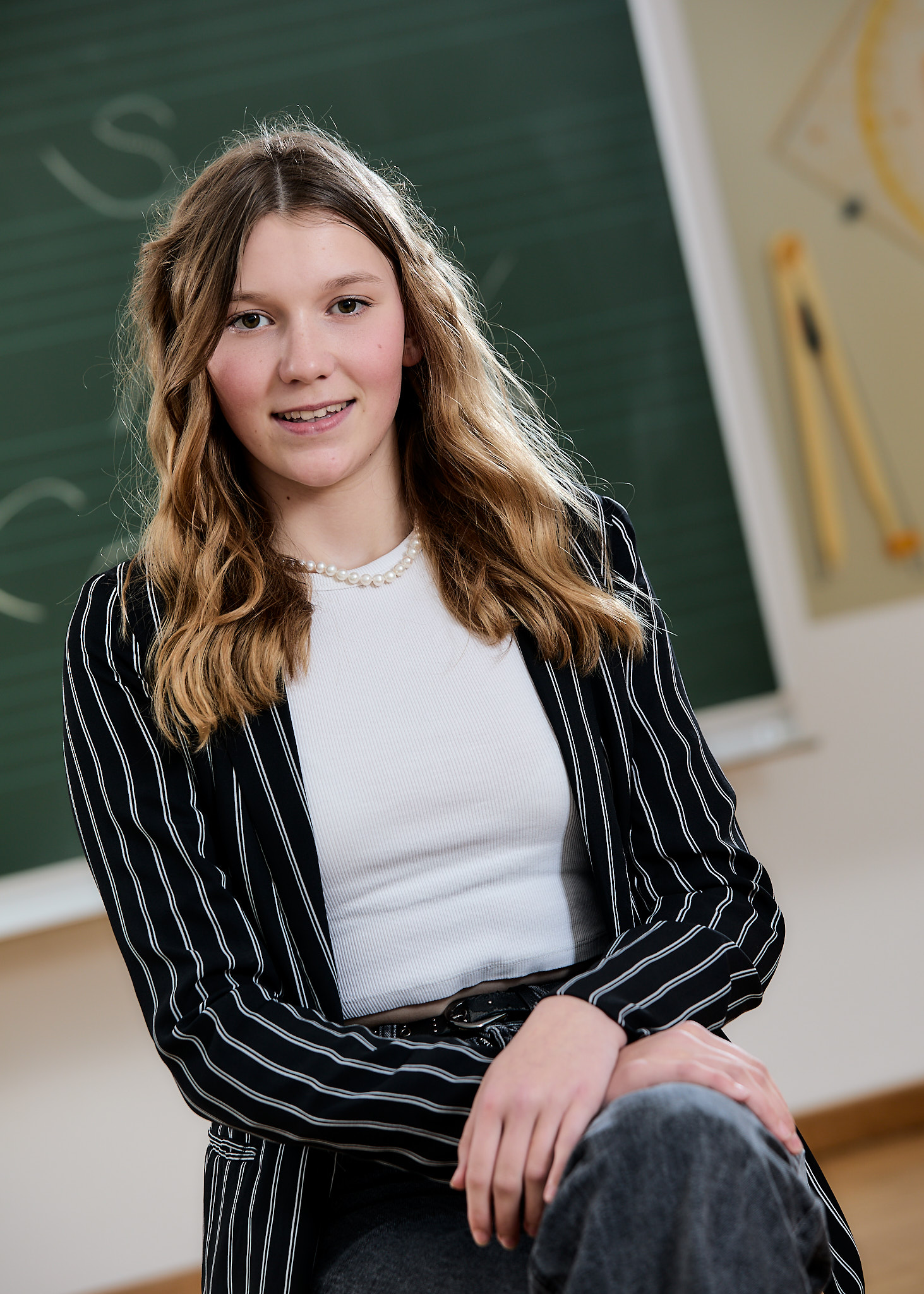 Portrait einer Schülerin, die vor der Schultafel sitzt. Schulfotografie.